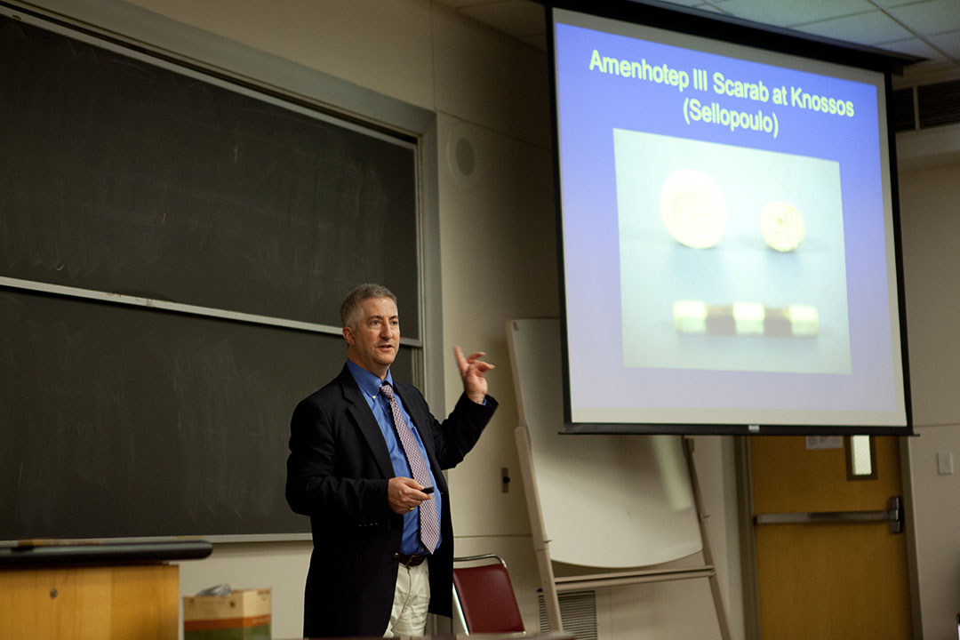 Eric Cline presenting in front of a slide showing Amenhotep III Scarab at Knossos