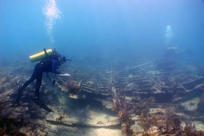 A diver underwater inspecting a ship wreck. Image via Wikimedia Commons.