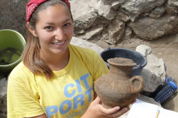 Student in a t-shirt holding an ancient pot at the Megiddo archaeological site